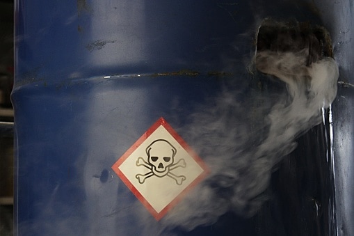 Gas tossici velenosi e acqua che fuoriescono da un barile di acciaio blu danneggiato, segno di materiale tossico sulla superficie del barile