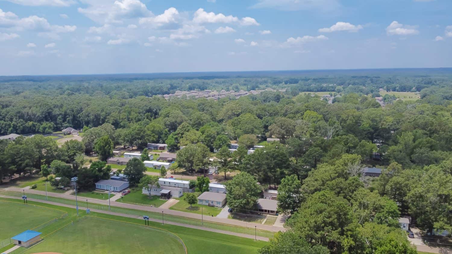 Grandi campi da baseball vicino a una fila di case fabbricate, modulari e mobili a Richland, contea di Rankin, sobborgo di Jackson nel Mississippi, quartiere di rigogliosi alberi verdi.  Alloggi convenienti di vista aerea