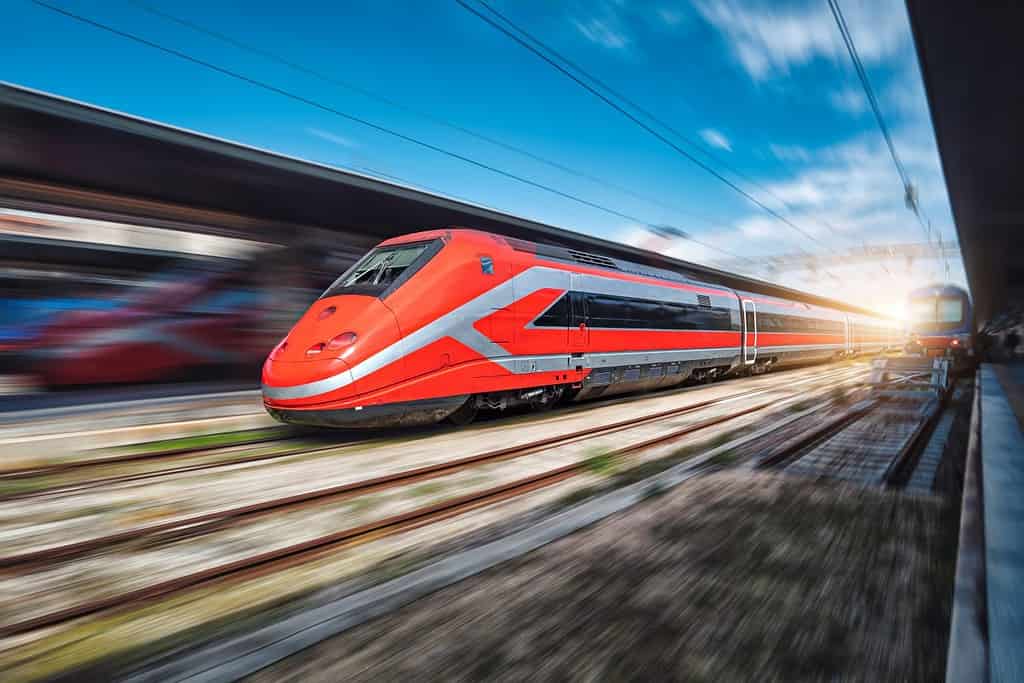 Treno ad alta velocità in movimento sulla stazione ferroviaria al tramonto.  Treno interurbano moderno rosso veloce e sfondo sfocato.  Piattaforma ferroviaria.  Ferrovia in Italia.  Commerciale.  Trasporto ferroviario passeggeri