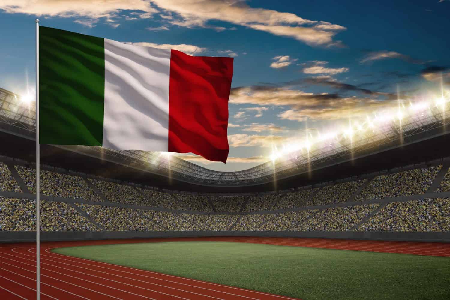 Bandiera italiana davanti ad uno stadio di atletica leggera con tifosi.