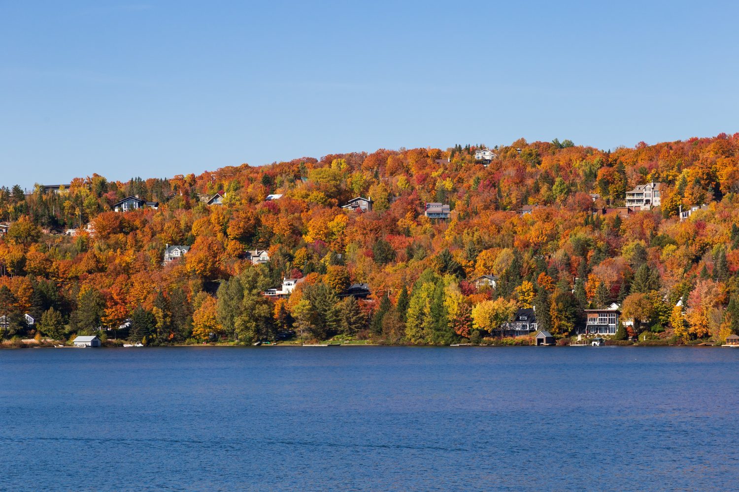 Case immerse nel colorato fogliame autunnale sul lato di una montagna che si affaccia su un lago, Lac-Beauport, Quebec, Canada
