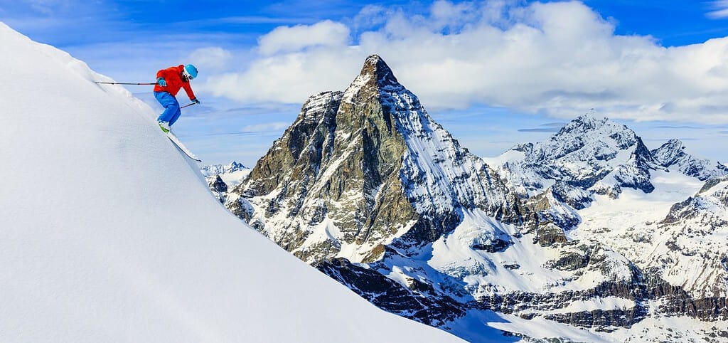 Sciatore che scia in discesa in alta montagna in neve fresca e polverosa.  Catena montuosa di neve con il Cervino sullo sfondo.  Regione delle Alpi di Zermatt Svizzera.