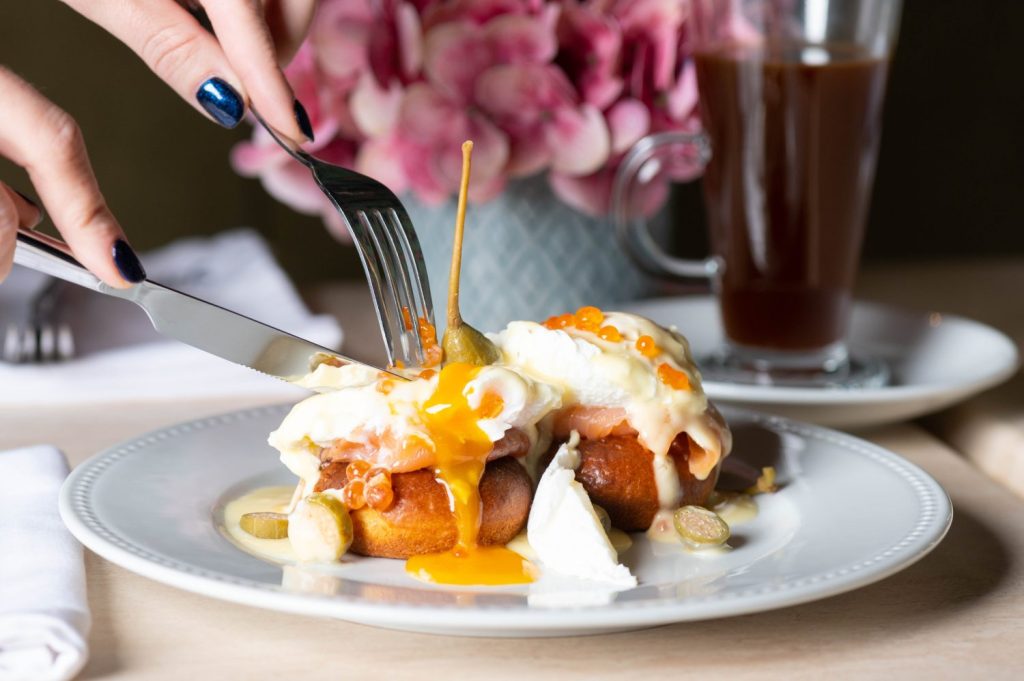 Ragazza che mangia uova alla Benedict con salmone affumicato, capperi e caviale di salmone per colazione