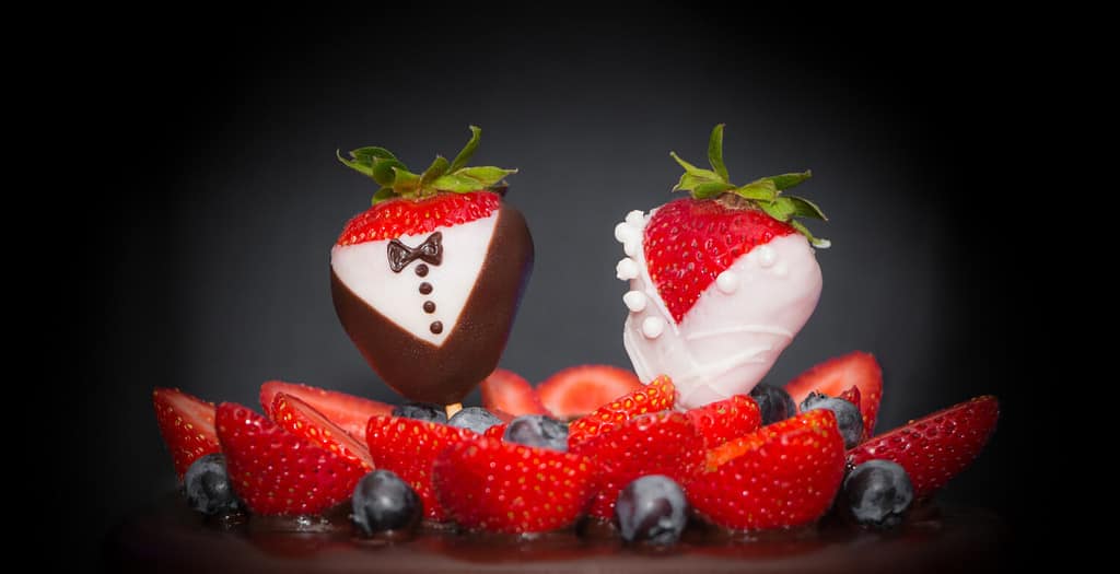 Sposo della sposa della coppia nuziale della fragola alla torta nuziale al cioccolato.  Dolciumi di lusso, arte, tendenza, matrimonio, fragole, abbellimento degli sposi, mirtilli e crema glassata.  Simbolo alimentare dell'amore