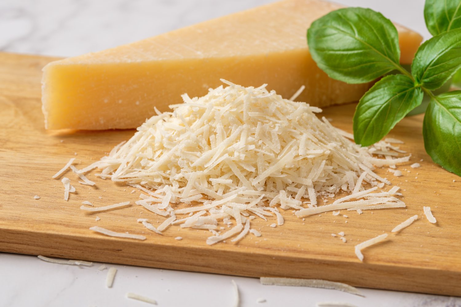 Grana Padano grattugiato su un tagliere.  Cuneo intero di parmigiano italiano e grattugiato con erba di basilico verde su sfondo di legno.  Delizioso formaggio a pasta dura.  Prodotto lattiero-caseario.  Vista frontale.