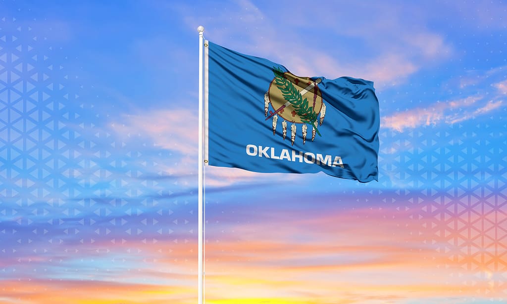 Bandiera dello stato dell'Oklahoma che scorre nella brezza.  Tramonto dietro la bandiera.