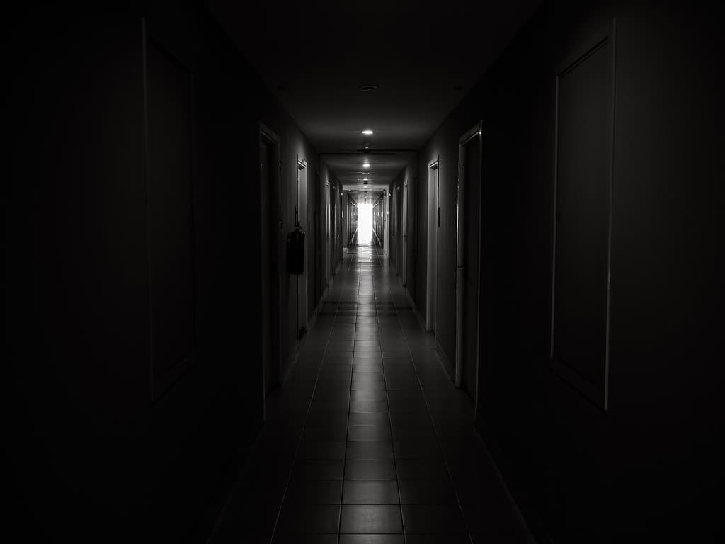 Corridoio scuro e misterioso nell'edificio.  Prospettiva della porta in un edificio solitario e tranquillo con passerella diretta verso la luce alla fine del percorso, in stile bianco e nero.  concetto di speranza, coraggio e paura.