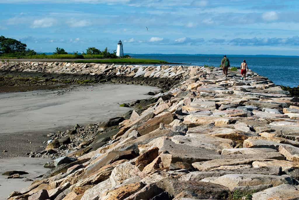 Giovane coppia che fa un'escursione lungo il frangiflutti roccioso verso la luce del porto di Black Rock che si collega all'isola di Fayerweather a Bridgeport, nel Connecticut.  È una delle sfide preferite di molti turisti a Seaside Park.