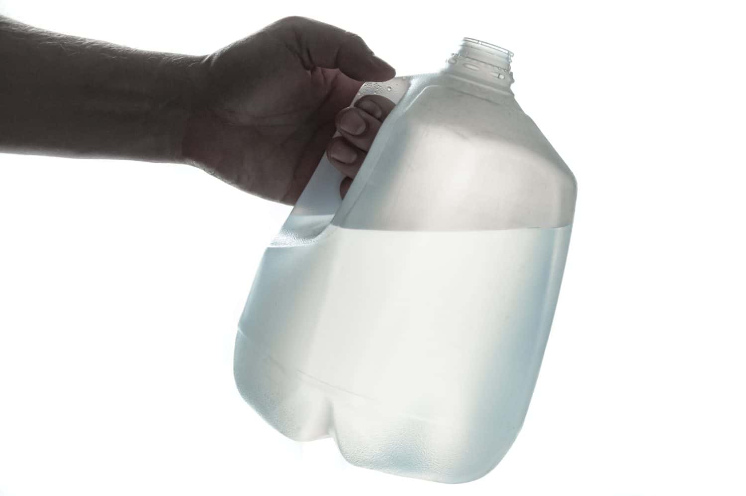 Mano che tiene una bottiglia di plastica da 1 gallone di acqua potabile;  sagoma su bianco.