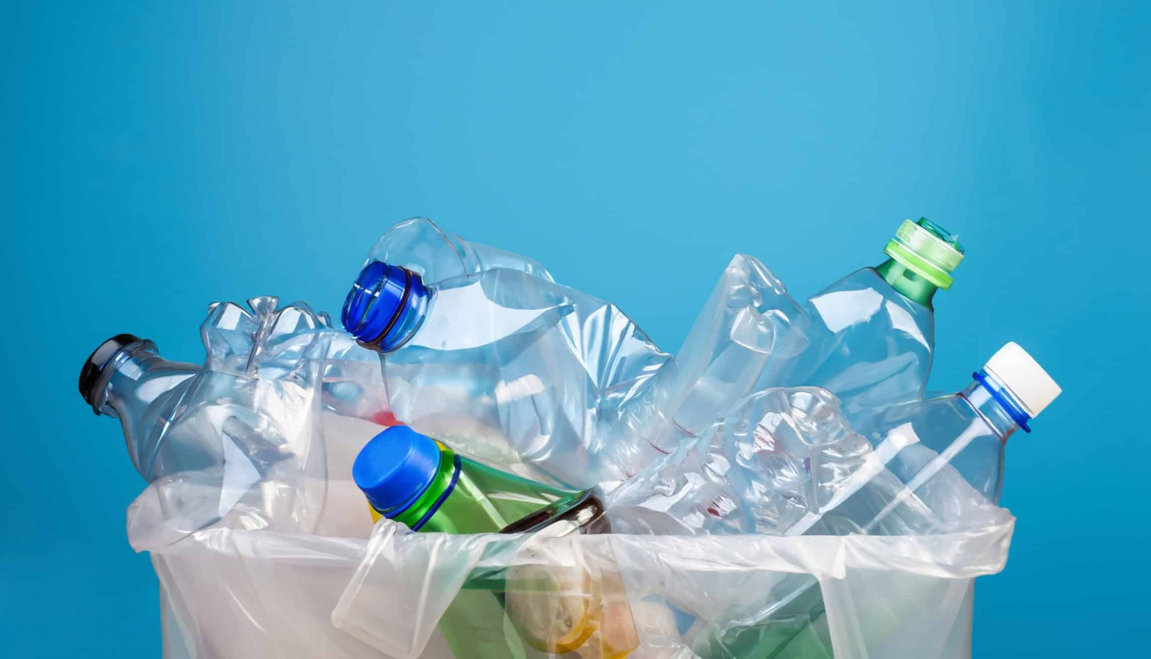 Bottiglie di plastica di scarto nel cestino su sfondo blu