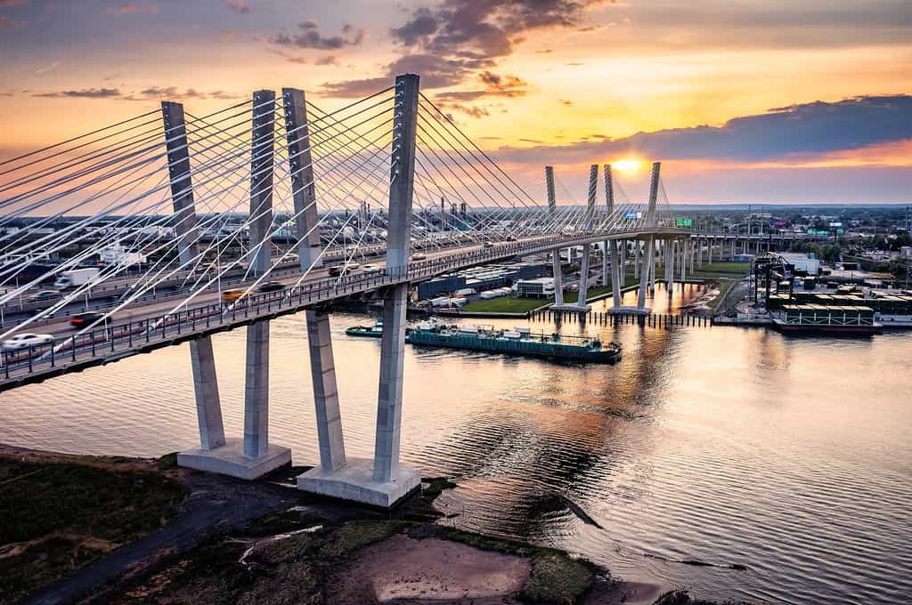 Veduta aerea del New Goethals Bridge al tramonto, che attraversa lo stretto di Arthur Kill tra Elizabeth, New Jersey e Staten Island, New York.  Una nave portacontainer naviga sotto il ponte.