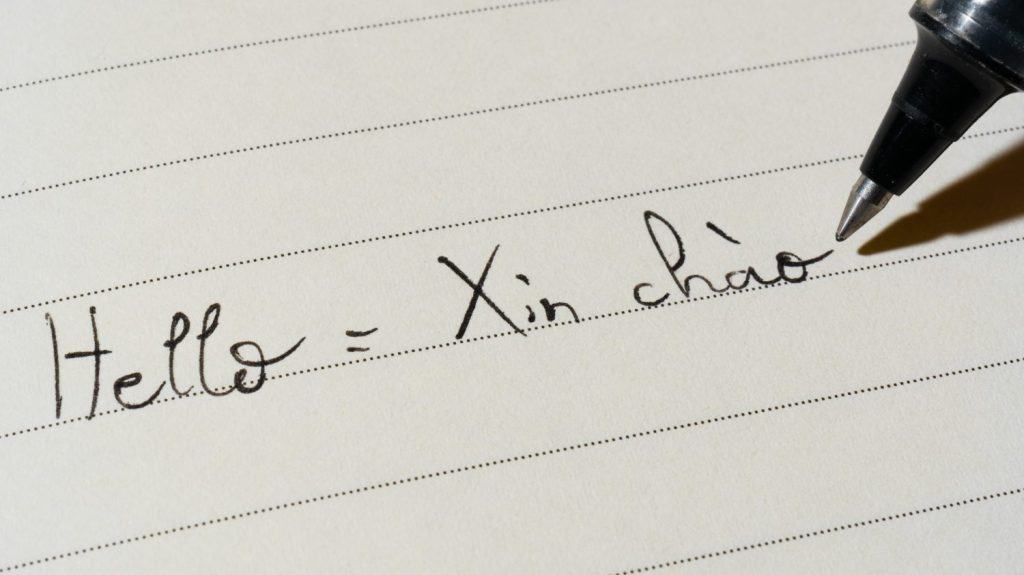 Studente principiante di lingua vietnamita che scrive la parola Ciao Xin Chao per i compiti su una ripresa macro di un notebook