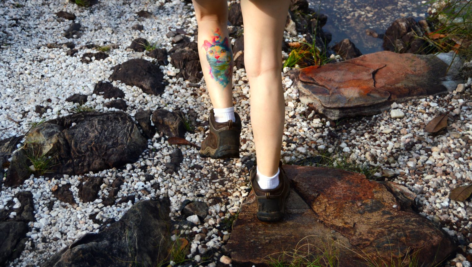 Donna con un tatuaggio di gatto acquerello sulla gamba che fa un'escursione su un sentiero di pietra