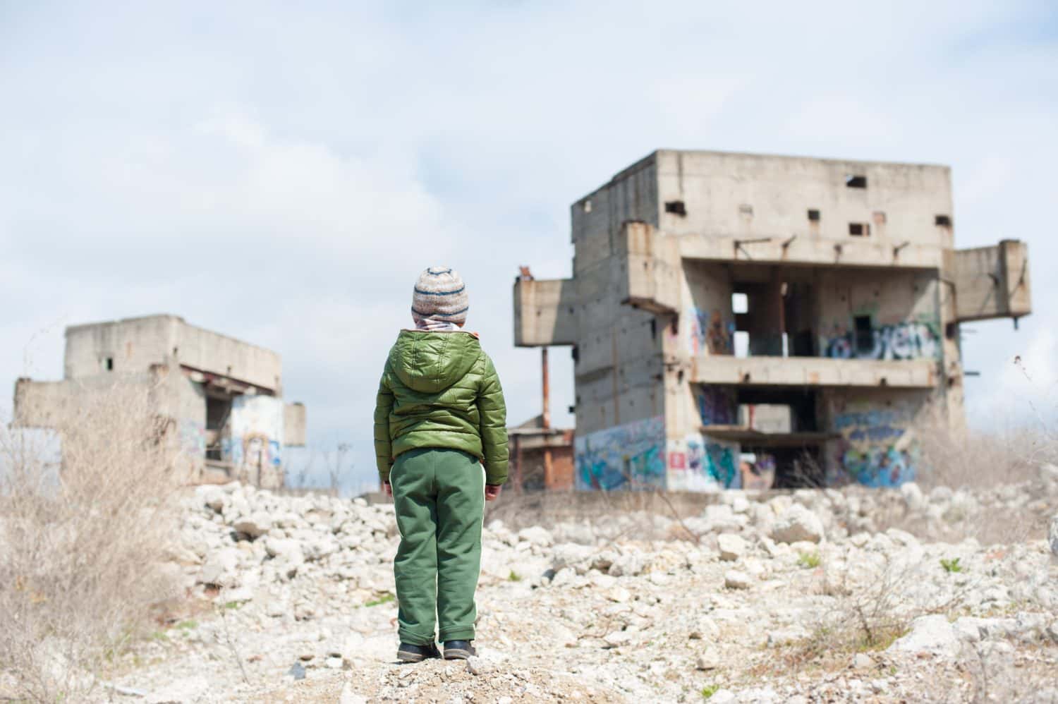 un bambino in giacca verde in piedi sulle rovine di edifici distrutti nella zona di guerra