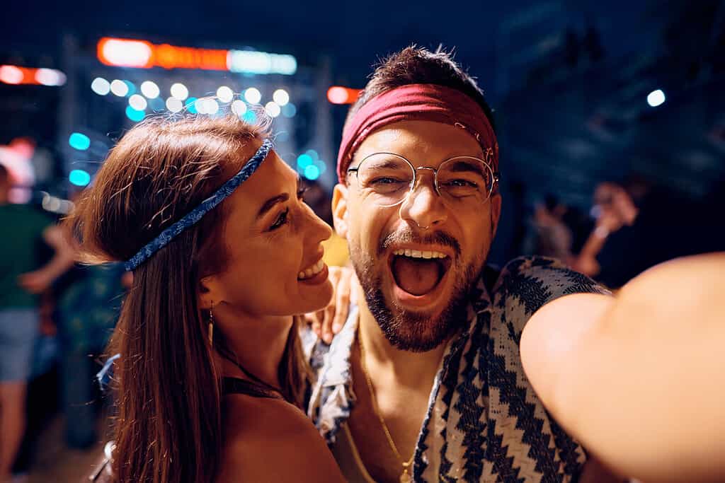 Coppia allegra coppia prendendo selfie mentre partecipa al festival di musica all'aperto di notte.