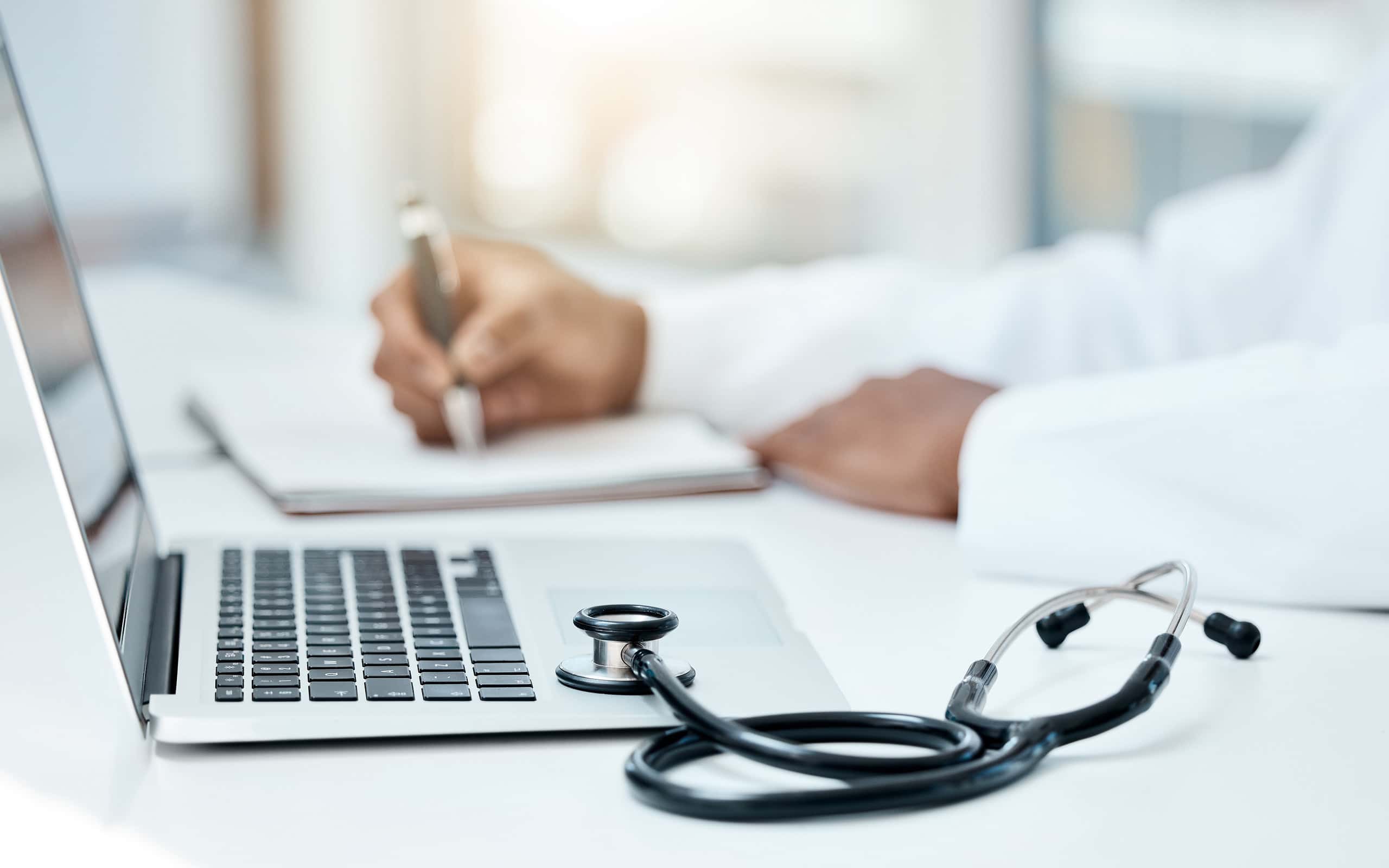 Laptop, stetoscopio e medico scrivono su un taccuino per la pianificazione della ricerca o l'innovazione della tecnologia medica nell'ufficio ospedaliero.  Operatore medico sanitario, appunti sul libro della strategia di ricerca e comunicazione online