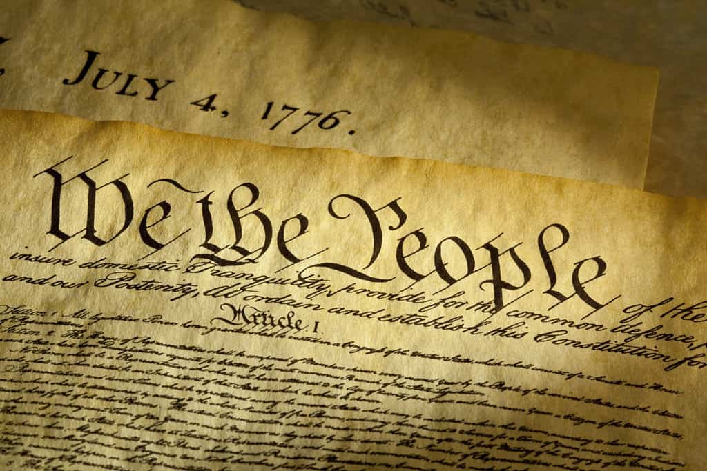 We the People è l'incipit del preambolo della Costituzione degli Stati Uniti.  Il documento sottostante è una copia della Dichiarazione di Indipendenza con la data 4 luglio 1776 in evidenza.