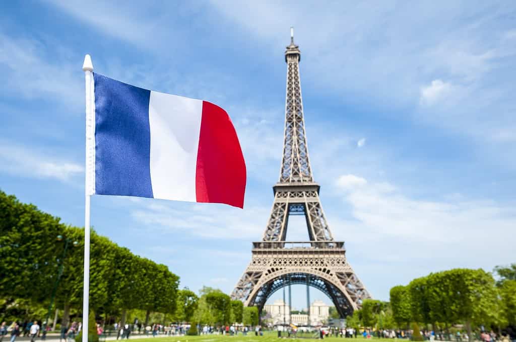 Bandiera francese che sventola nel cielo primaverile azzurro brillante di fronte alla Torre Eiffel a Parigi, Francia