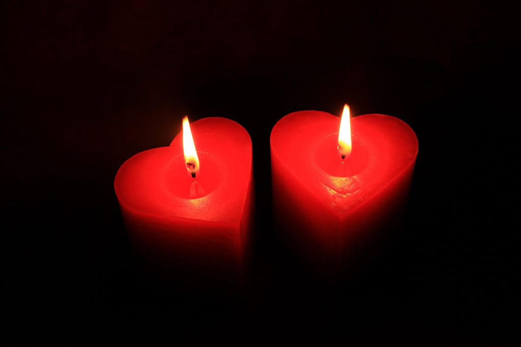 Due fiamme che bruciano nell'oscurità.  Due candele rosse a forma di cuore su sfondo nero