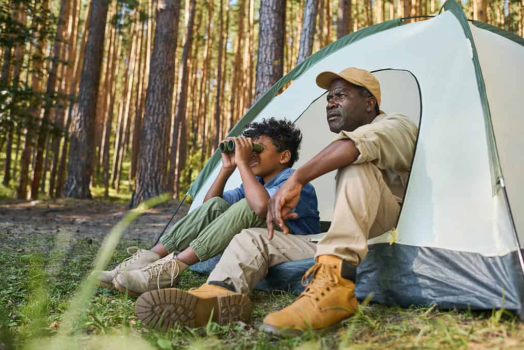 Carino ragazzo afroamericano che guarda attraverso il binocolo mentre era seduto in tenda