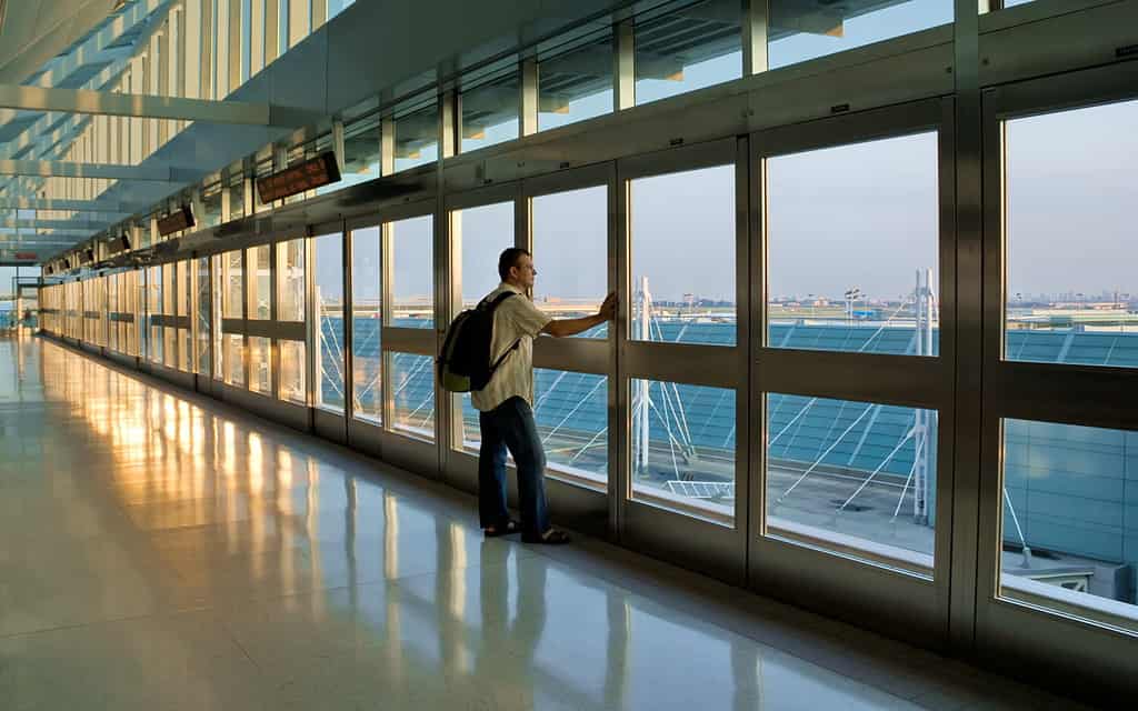 Uomo in piedi accanto a una finestra e in attesa del suo volo, l'Aeroporto Internazionale Pearson di Toronto, Canada.