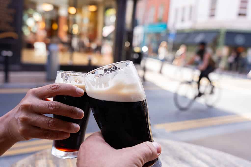 Primo piano di due mani che si brindano a vicenda con birre Guinness in una strada centrale di Dublino divertendosi in una bella mattina autunnale