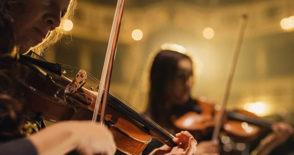 Primo piano cinematografico del violinista dell'Orchestra Sinfonica Professionale che suona sul teatro classico con palco a tendina durante il concerto musicale.  Artisti che suonano musica per il pubblico