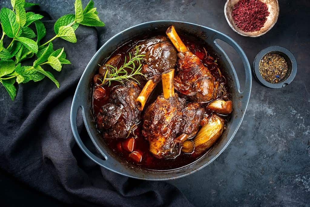 Stinco di agnello brasato tradizionale in stile moderno cotto lentamente in salsa al vino rosso con scalogno e carote offerto come vista dall'alto in uno stufato di design