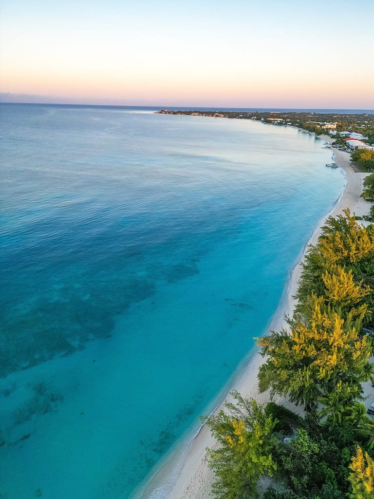 Veduta aerea dell'alba dorata a Seven Mile Beach, Grand Cayman, Isole Cayman, una destinazione tropicale nei Caraibi con una vista rilassante di condomini sulla spiaggia, hotel e vegetazione lussureggiante