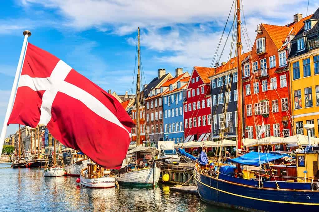 Vista iconica di Copenaghen.  Famoso vecchio porto di Nyhavn nel centro di Copenhagen, Danimarca durante la giornata di sole estivo con la bandiera della Danimarca in primo piano.