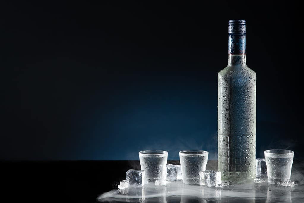 Bottiglia ghiacciata di vodka con bicchierini su sfondo blu scuro con spazio per la copia.
