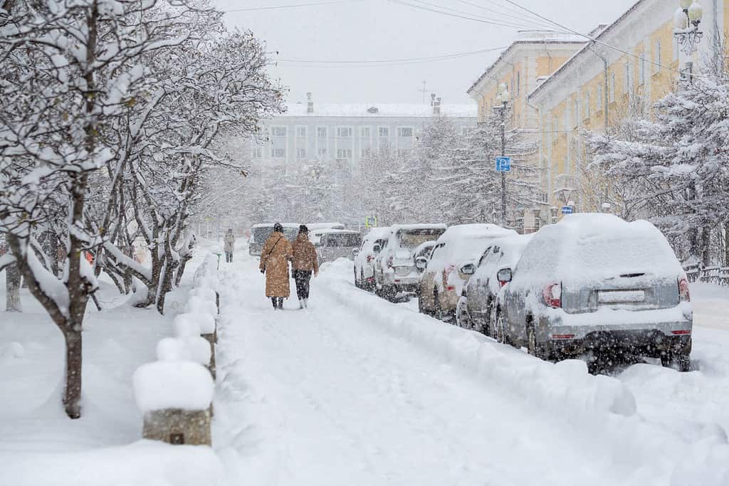 Strada cittadina innevata durante una forte nevicata.  Tanta neve sui marciapiedi, sulle auto e sui rami degli alberi.  Le donne camminano per la città invernale.  Tempo freddo e nevoso.  Magadan, Siberia, Estremo Oriente russo.