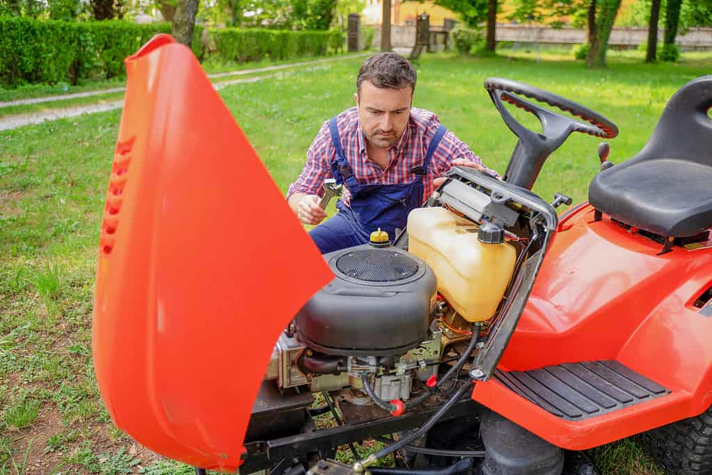 Un giardiniere che falcia l'erba e risolve il problema al motore del tosaerba