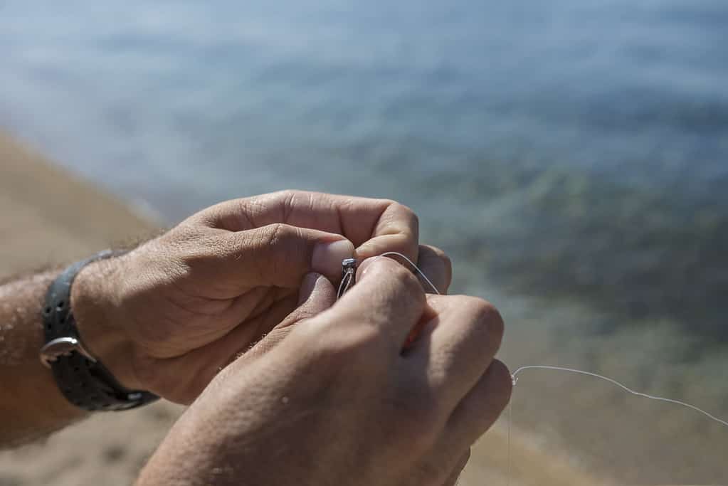 Un uomo annoda un amo da pesca e un piombo sulla spiaggia