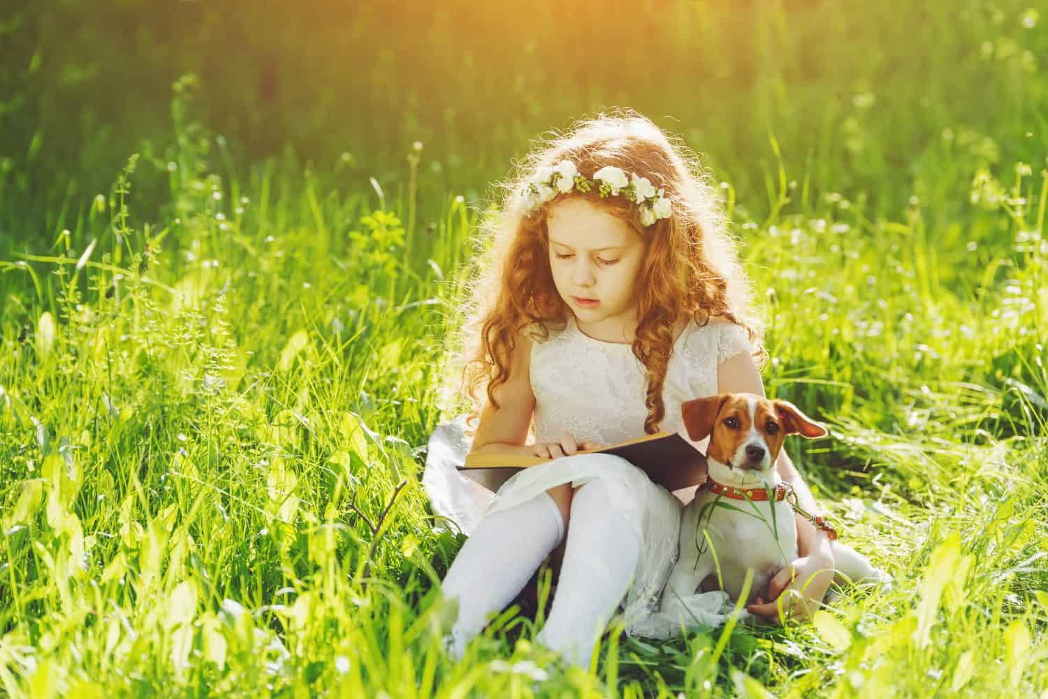 Bambina che legge un libro con il suo amico cucciolo di cane all'aria aperta.