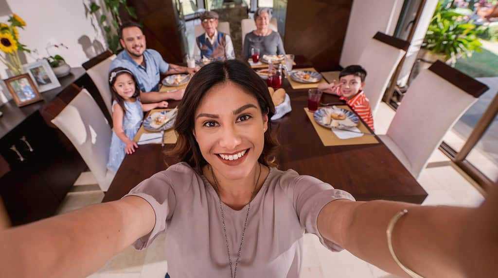 Bella donna latina si fa un selfie con il cellulare per tenere insieme il ricordo di nonni, genitori e nipoti a tavola.  Famiglia latina.