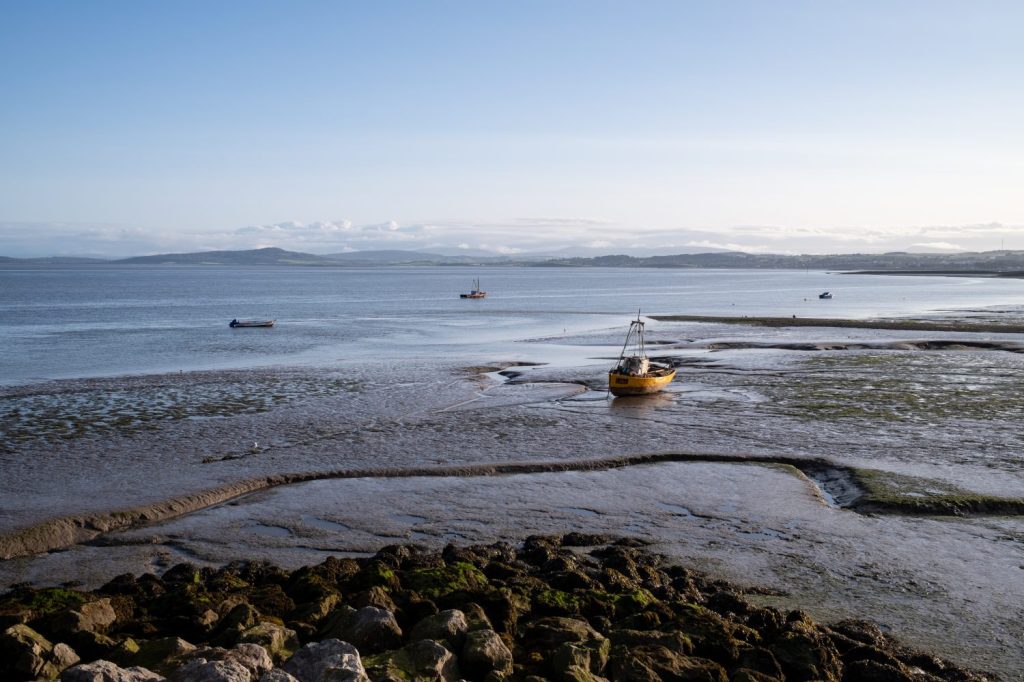 Barca arenata sulla riva, con altri in mare, a Morecambe Bay a Morecambe, Lancashire, Regno Unito