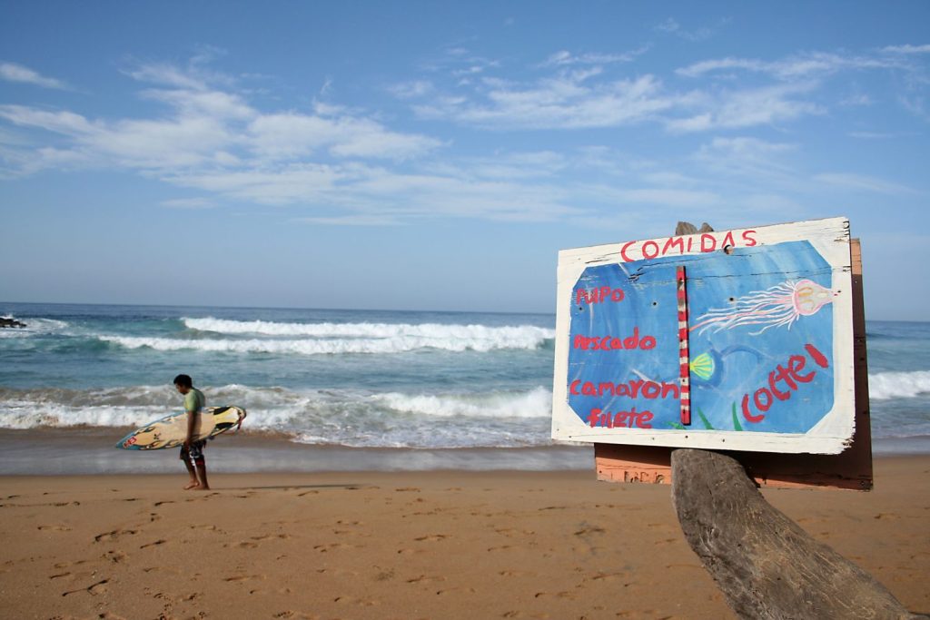 Surfista che trasporta la sua tavola a Zipolite Beach, Oax., Messico.