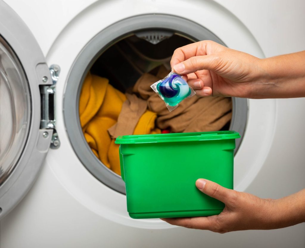 Donna che mette la capsula del detersivo per bucato nella lavatrice all'interno, primo piano. Gel ecologico per bucato colorato in capsula.  Lavare i vestiti. Il concetto di lavaggio e pulizia