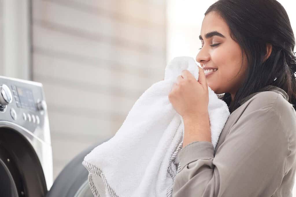 Donna annusante, pulente o felice con lavanderia, macchina e casa per vestiti, tessuti e pulizie.  Profumo, persona femminile e articoli più puliti per lavare in lavanderia con routine, sorriso e servizio