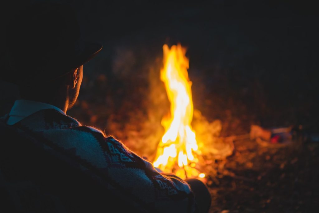 Momento tranquillo e tranquillo nella notte accanto al fuoco, messa a fuoco morbida.  L'uomo con il tradizionale poncho e cappello dei nativi americani si siede accanto al fuoco nel bosco