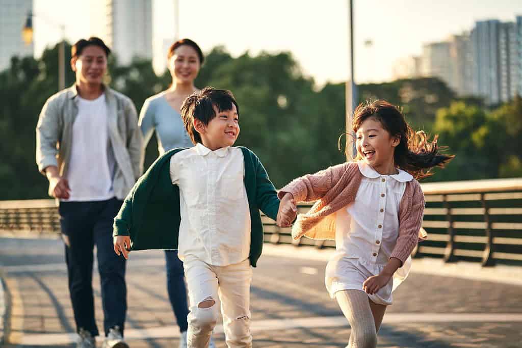famiglia asiatica felice con due bambini che camminano sul ponte pedonale nel parco cittadino