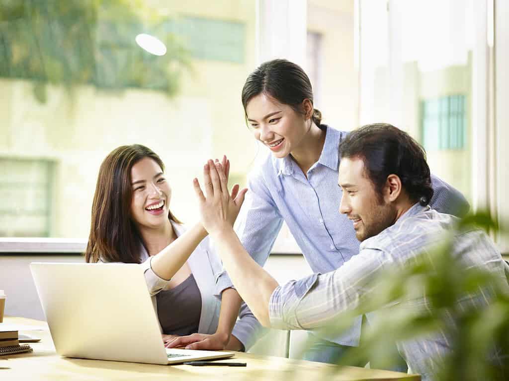 Giovane imprenditore asiatico che dà il cinque a un collega in ufficio celebrando i successi e i traguardi raggiunti.