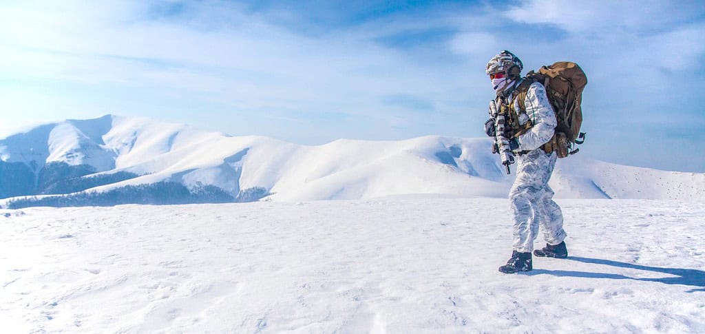 Un militare in mimetica invernale da qualche parte nell'Artico. Indossa un gilet, uno zaino, soffre il freddo estremo, il vento forte, ma resiste mentre la missione continua, correndo e muovendosi attraverso il deserto innevato