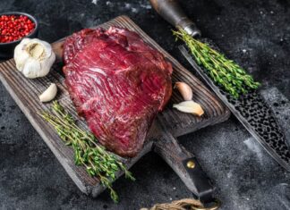 Carne di cervo cruda su un tagliere con erbe aromatiche. Sfondo nero. Vista dall'alto