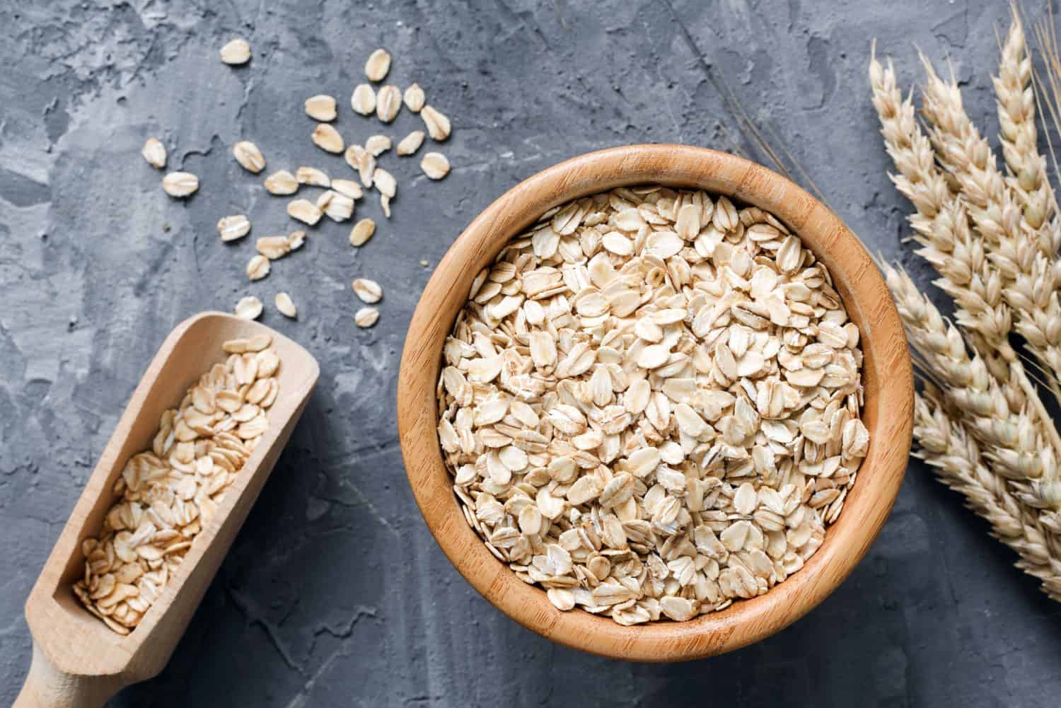 Fiocchi d'avena o fiocchi d'avena in ciotola di legno e spighe di grano dorate su fondo di pietra. Vista dall'alto, orizzontale. Stile di vita sano, alimentazione sana, concetto di cibo vegano