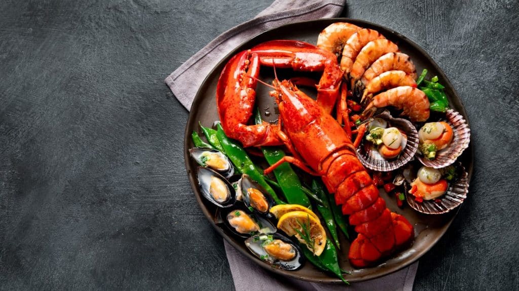 Grande aragosta rossa sul piatto con gamberi e cozze al limone, salsa di pesto e pane. Concetto di frutti di mare. Vista dall'alto, copia dello spazio