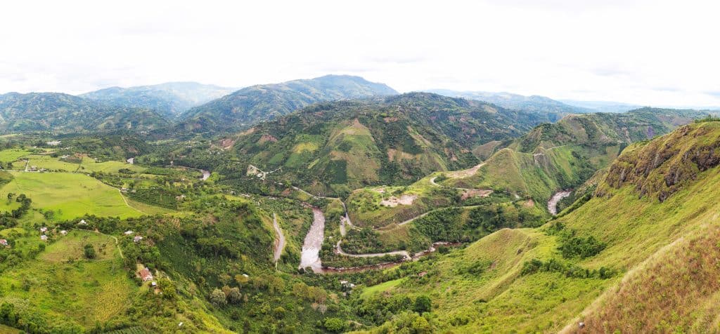 Vista con verdi colline che sembrano pascolate attorno ad un fiume con uno sfondo di basse montagne.