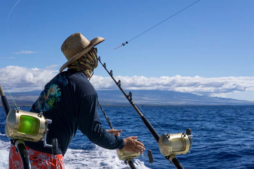Grande Isola, Hawaii, Stati Uniti. Pesca maschile su una barca. Battuta di pesca durante le vacanze. Acqua blu intenso, bel cielo. Colpo d'azione.